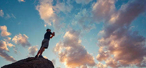 Silhouette of a man on a pinnacle praying to the sunset sky